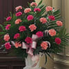 Tall arrangement of pink and dark pink carnations with ribbons in a white urn