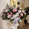 Tall pink and white sympathy arrangement in white urn with memorial ribbon on a pedestal