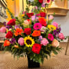 Tall mixed arrangement of bright roses, gerbera daisies, and sunflowers in a black vase