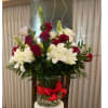 Tall arrangement of red roses and white lilies in a clear glass vase with a red bow