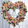 Heart-shaped floral wreath on a black stand with pink, peach, and purple flowers