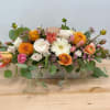 Low rectangular flower arrangement with orange, white, and pink blooms in a wooden box
