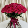 Hand-tied bouquet of bright pink roses with exposed stems and a matching ribbon on a white table.