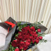 Large bouquet of red roses wrapped in black paper with a red ribbon, resting on a gold table.