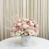 Round arrangement of blush, pink, and cream roses in a white hatbox-style container