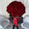 Oversized bouquet of red roses wrapped in black paper with gold trim and a red ribbon, held between two white chairs