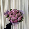 Handheld bouquet of pink ranunculus wrapped in lavender paper