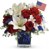 Red roses and white lilies in a blue glass vase with a small American flag.