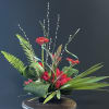 Red gerbera daisies in a black container with tall willow branches