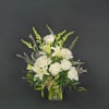 White roses, lilies, and snapdragons arranged in a clear glass vase against a dark background