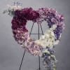 Heart-shaped floral wreath on a black stand with purple, pink, and white blooms