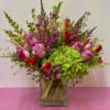 Pink roses and red tulips arranged with green hydrangea in a glass vase.