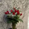 This is a vase of a dozen red roses elegantly arranged in