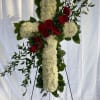 Tall white floral cross with red roses and greenery displayed on a metal easel