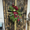 Tall cross-shaped standing spray with red roses and greenery on a wooden easel.