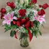 Bouquet of red roses and pink lilies in a glass vase with a red ribbon