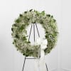 White floral wreath on a black stand with a white ribbon bow