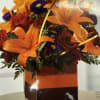 Orange lilies and red roses in a clear vase with gold ribbon