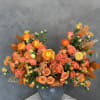 Orange and coral roses in a gray vase with autumn leaves