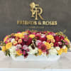 Large mixed flower arrangement in a white rectangular container with apples