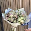 Bouquet of pale roses and pink filler flowers wrapped in cream paper