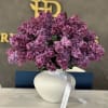 Purple lilac bouquet in a white vase with a ribbon