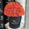 Round bouquet of orange and pink roses in a black hat box