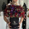 Large bouquet of red and purple flowers in a black box with black feathers.