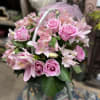 Pink roses and lilies arranged in a basket with a tulle bow