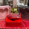 Red roses in a clear heart-shaped box with pink and black heart boxes nearby