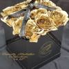 Gold roses arranged in a black gift box with a ribbon.