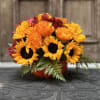 Bouquet of sunflowers, orange roses, and red flowers in a red container