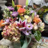 Mixed bouquet of roses, lilies, hydrangea, and daisies in a pale vase