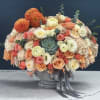 Mixed bouquet of peach, cream, and orange flowers in a gray vase