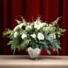 White roses in a glass vase with dense evergreen foliage