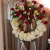 Standing floral wreath with red roses and white flowers on a ribboned easel
