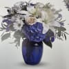 White lilies and purple flowers arranged in a blue glass vase
