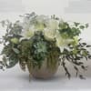 White lilies and roses in a round vase with trailing greenery