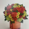 Bouquet of red roses, yellow blooms, and green flowers in an orange vase