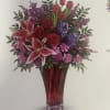Mixed bouquet of red, pink, and purple flowers in a tall red vase