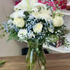 White lilies, roses, and daisies in a glass vase with blue baby's breath