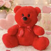 Red plush teddy bear with a satin bow sitting on a soft blanket