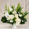White floral arrangement in a white pedestal vase with orchids and lilies