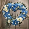 Heart-shaped floral wreath of blue hydrangeas and white roses on a stand