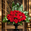 Red rose arrangement in a black pedestal vase with large green leaves