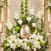 White lilies and roses arranged around a gold urn with green accents.