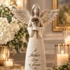 Angel figurine holding a rose beside white flowers and lit candles