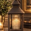 Bronze lantern with a memorial candle and a potted plant beside it.