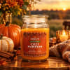 Pumpkin-scented candle in a glass jar on a wooden table with autumn decor