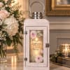 Wooden lantern with a lit candle and floral print beside a pink-and-white bouquet